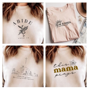 May include: Four different designs for t-shirts featuring Christian themes. The first design says "ABIDE" with a floral design and the text "JOHN 15". The second design says "HE IS RISEN" with a sunburst design and the text "MATTHEW 28:6". The third design features a nativity scene with the text "A thrill of hope, the weary world rejoices". The fourth design says "this mama prays" with a floral design.