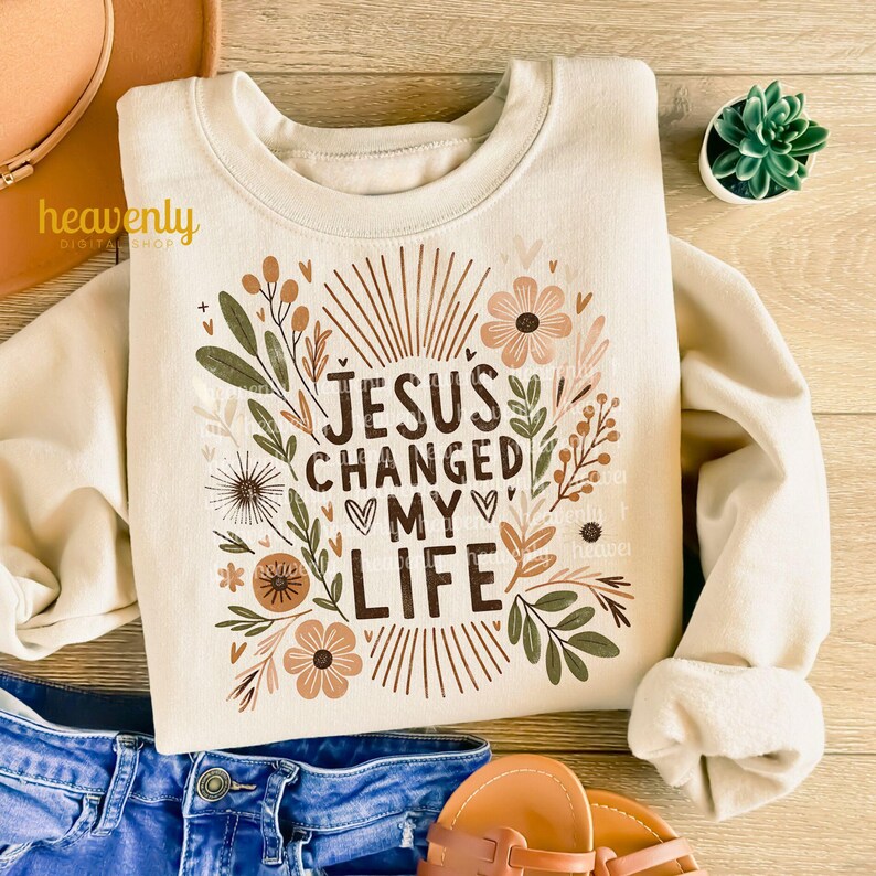 May include: A beige sweatshirt with a floral design and the text "JESUS CHANGED MY LIFE" in brown lettering.