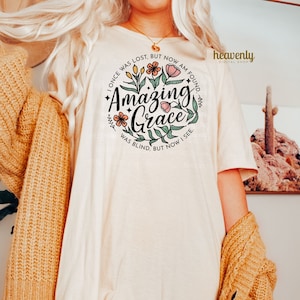May include: A white t-shirt with a floral design and the text "I once was lost, but now am found. Amazing Grace. Was blind, but now I see."