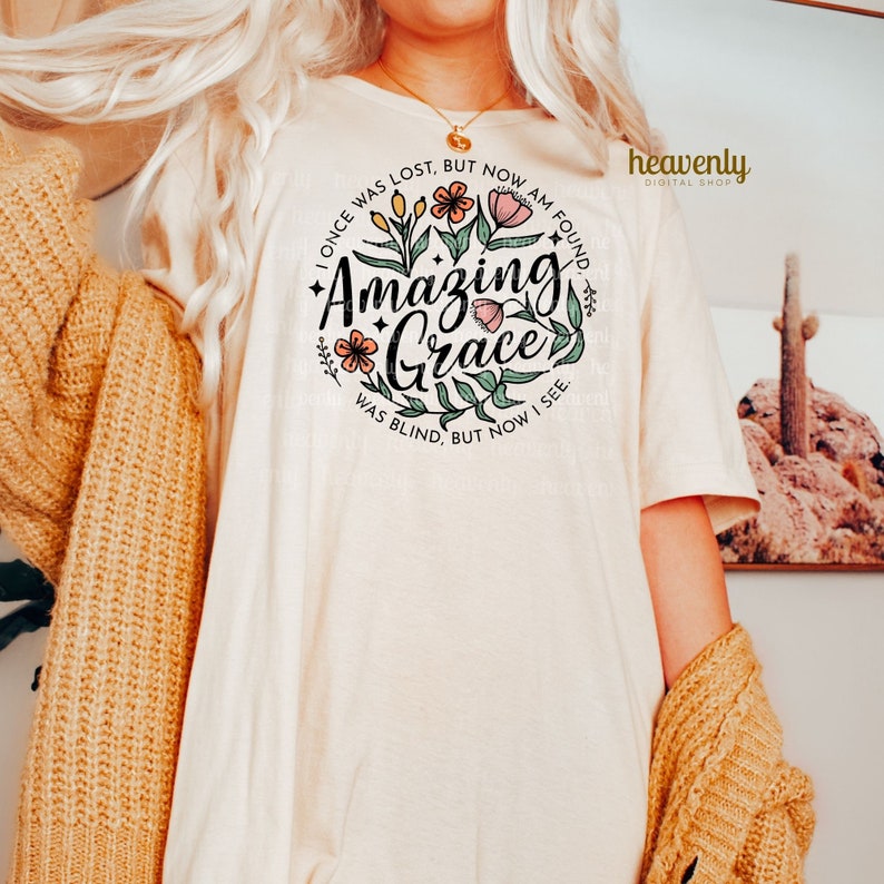 May include: A white t-shirt with a floral design and the text "I once was lost, but now am found. Amazing Grace. Was blind, but now I see."