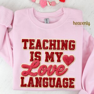 K&ouml;nnte beinhalten: Hellrosa Sweatshirt mit dem Text "TEACHING IS MY LOVE LANGUAGE" in roter und goldener Schrift. Eine rote Herzgrafik befindet sich neben dem Wort "LOVE". Das Sweatshirt hat lange &Auml;rmel und einen Rundhalsausschnitt.