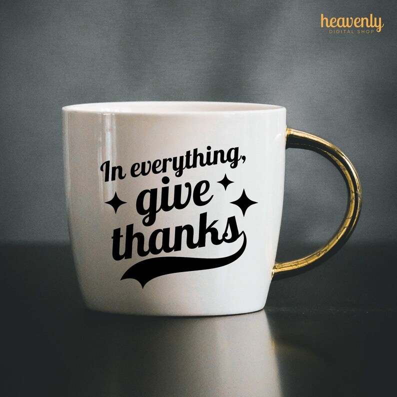 May include: White ceramic mug with a gold handle. The mug has a black graphic that says "In everything, give thanks" with two small stars on either side of the word "give".