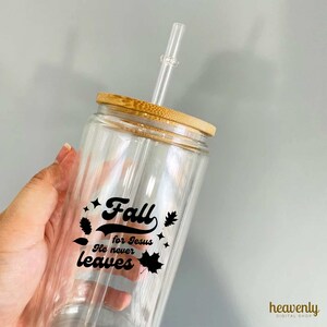 Op de afbeelding: Een doorzichtige glazen beker met een bamboe deksel en een zwart-witte afbeelding met de tekst "Fall for Jesus He never leaves". De beker heeft een doorzichtige glazen rietje.