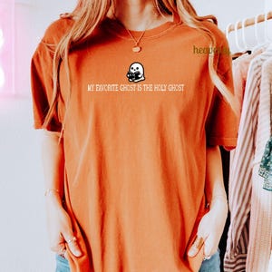 K&ouml;nnte beinhalten: Ein rostfarbenes T-Shirt mit einem wei&szlig;en Geistermotiv und dem Text "My favorite ghost is the Holy Ghost".