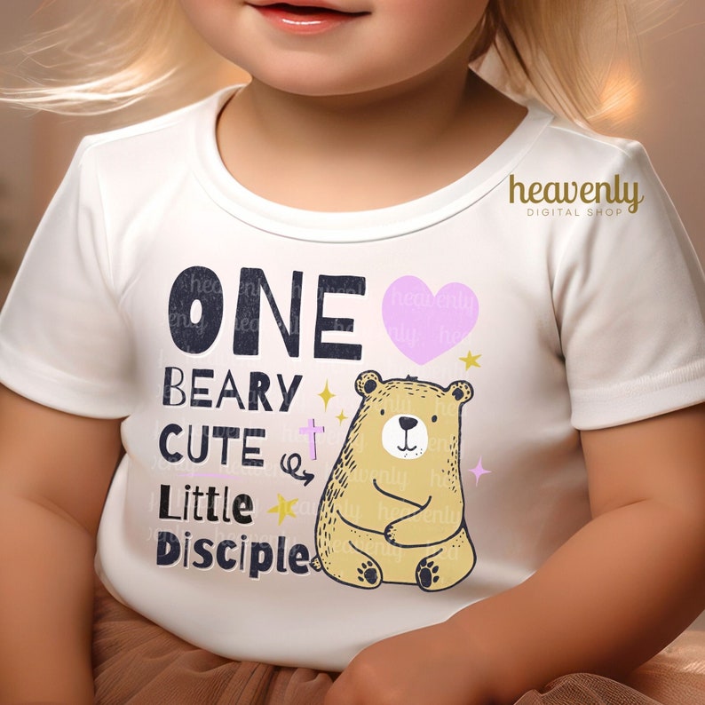 May include: White onesie with a pink heart, a brown bear, and the text "ONE BEARY CUTE Little Disciple".