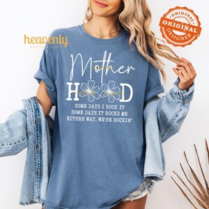 May include: A blue t-shirt with the text "Mother Hood" in white with a floral design and the text "Some days I rock it, some days it rocks me, either way, we're rockin'" in white.