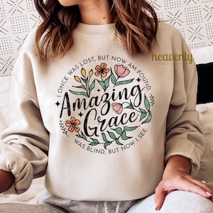 May include: A beige sweatshirt with a floral design and the text "I once was lost, but now am found. Amazing Grace. Was blind, but now I see."