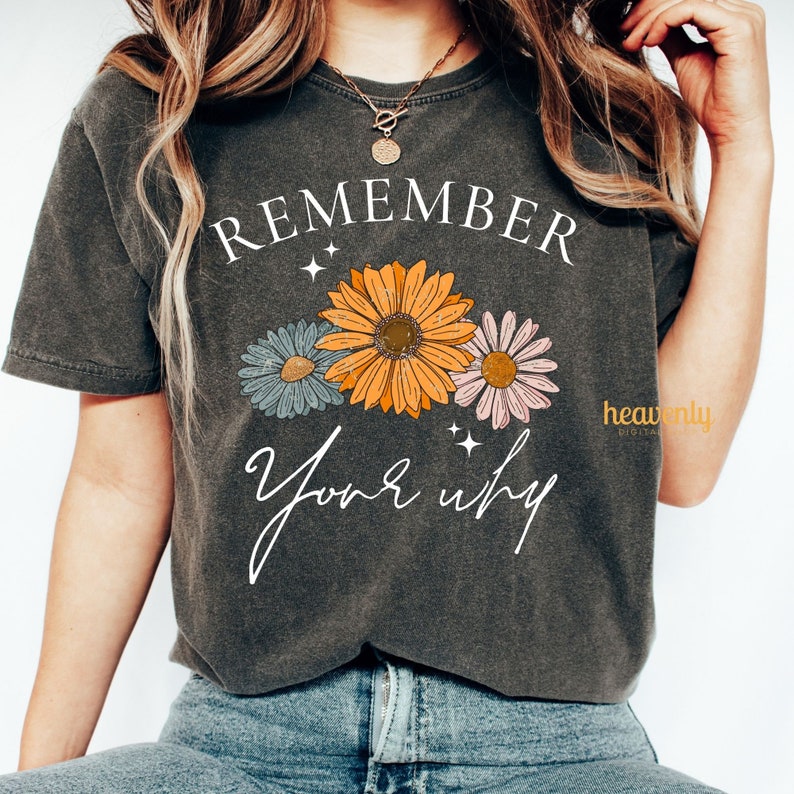 K&ouml;nnte beinhalten: Ein dunkelgraues T-Shirt mit dem Text "REMEMBER your why" in Wei&szlig;. Der Text ist von drei stilisierten Blumen in Orange, Rosa und Blau umgeben.