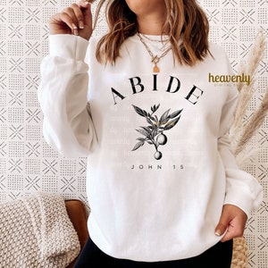 May include: White sweatshirt with black text that reads "ABIDE JOHN 15" and a black and gold floral design.