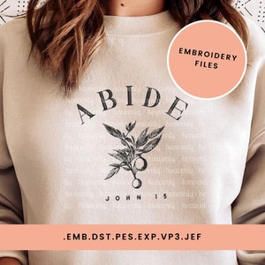 May include: A beige sweatshirt with black embroidery that reads "ABIDE JOHN 15" with a floral design. The text "EMBROIDERY FILES" is in a peach-colored circle at the top right corner of the image. The text ".EMB.DST.PES.EXP.VP3.JEF" is at the bottom of the image.