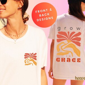 以下が含まれることがあります： 白いTシャツに、背面に花柄のデザインと「grow in grace」の文字がプリントされています。Tシャツの前面には、より小さな花柄のデザインが施されています。