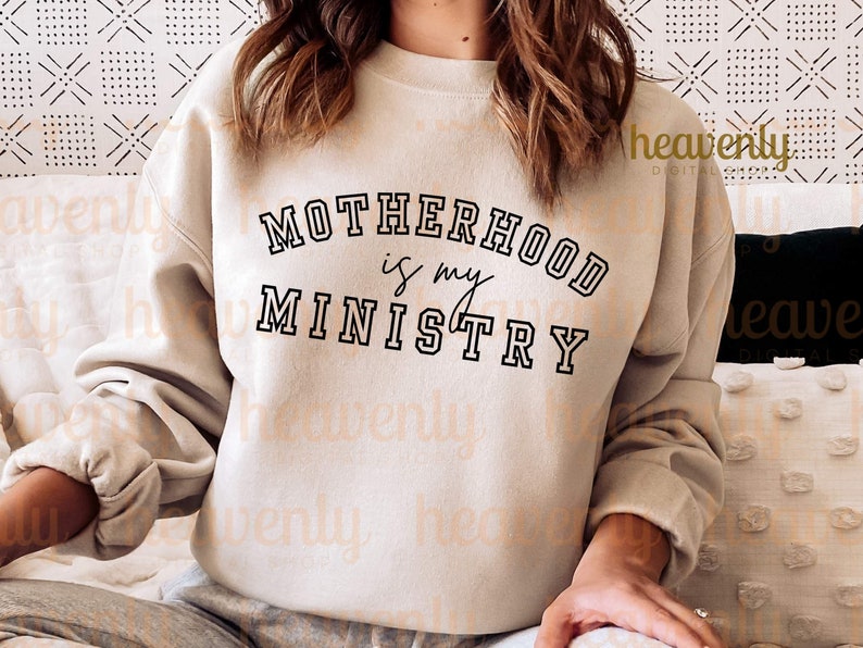 Pu&ograve; includere: Una felpa beige con il testo "MOTHERHOOD is my MINISTRY" in lettere nere.