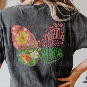 Puede incluir: Una camiseta negra con un dise&ntilde;o de mariposa colorido y el texto "Amazing Grace" en letras rosa y verde.