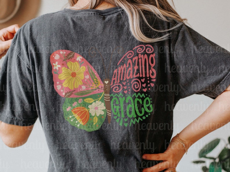 Puede incluir: Una camiseta negra con un dise&ntilde;o de mariposa colorido y el texto "Amazing Grace" en letras rosa y verde.