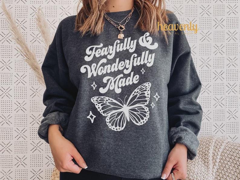 Pu&ograve; includere: Felpa grigio scuro con la scritta "Fearfully & Wonderfully Made" e una grafica a farfalla bianca. Il design include quattro piccoli diamanti. La felpa ha maniche lunghe e girocollo.