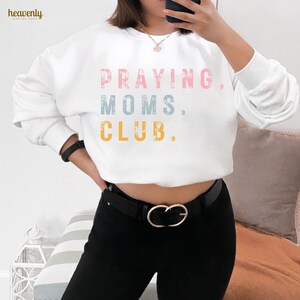 May include: White sweatshirt with the text "PRAYING. MOMS. CLUB." in pink, blue, and yellow lettering.