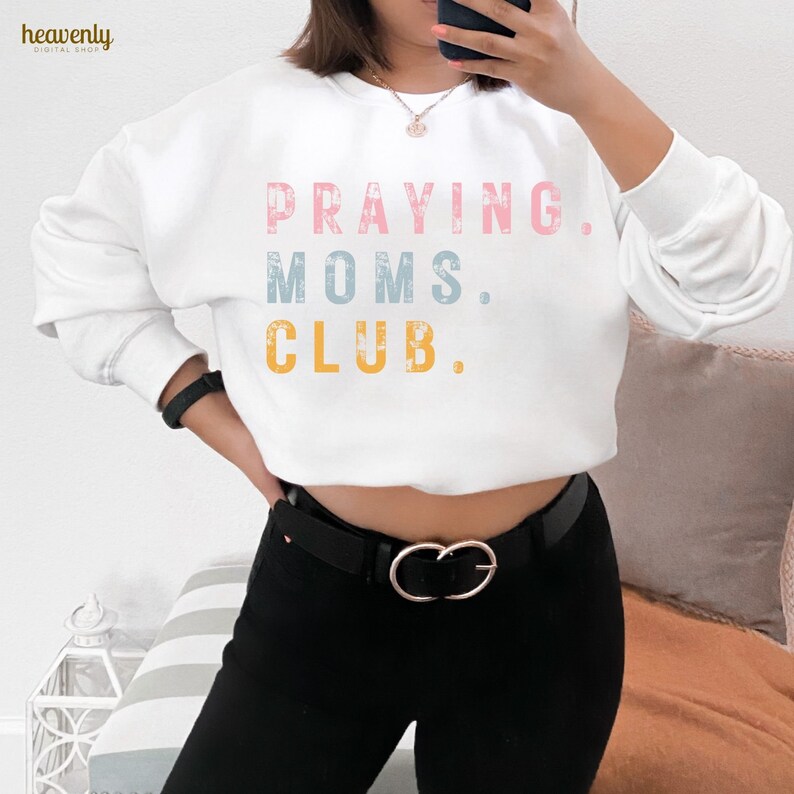 May include: White sweatshirt with the text "PRAYING. MOMS. CLUB." in pink, blue, and yellow lettering.