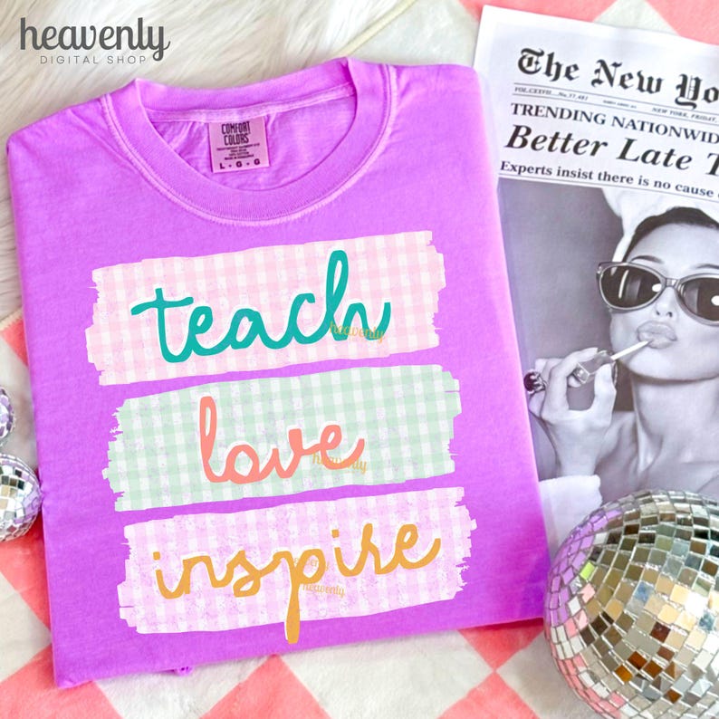 May include: A lilac Comfort Colors t-shirt with the words "teach love inspire" in teal, coral, and orange script. The words are on top of pastel gingham patterns. A newspaper and disco ball are in the background.