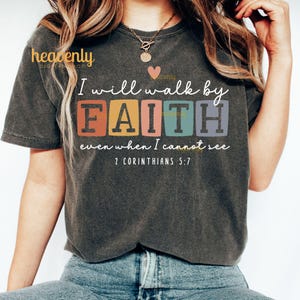 May include: A dark gray t-shirt with a colorful graphic that reads "I will walk by FAITH even when I cannot see 2 Corinthians 5:7".
