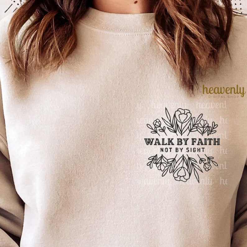 Puede incluir: Una sudadera beige con un dise&ntilde;o gr&aacute;fico negro que dice "Walk by Faith Not by Sight" rodeado de elementos florales.