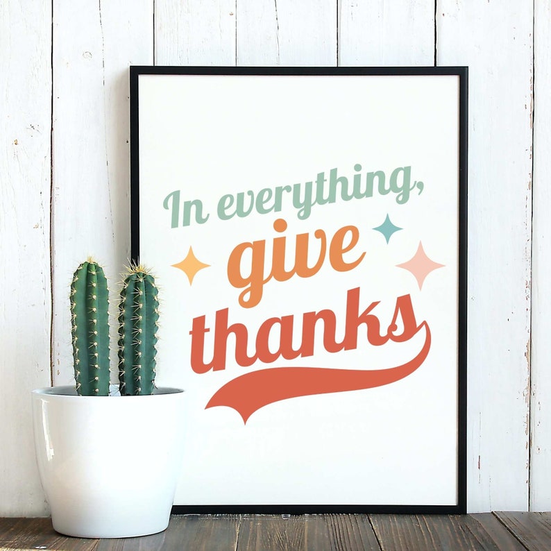 May include: A framed print with a white background and black frame. The print features the text "In everything, give thanks" in a colorful retro font with a red, orange, and yellow color scheme. The text is set against a white background with a red, orange, and yellow color scheme.