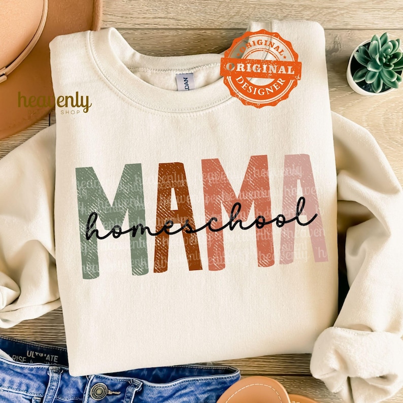 Puede incluir: Una sudadera de color crema con el texto "MAMA homeschool" en letras coloridas y texturizadas. Las letras son en tonos de verde, naranja, rojo y rosa.