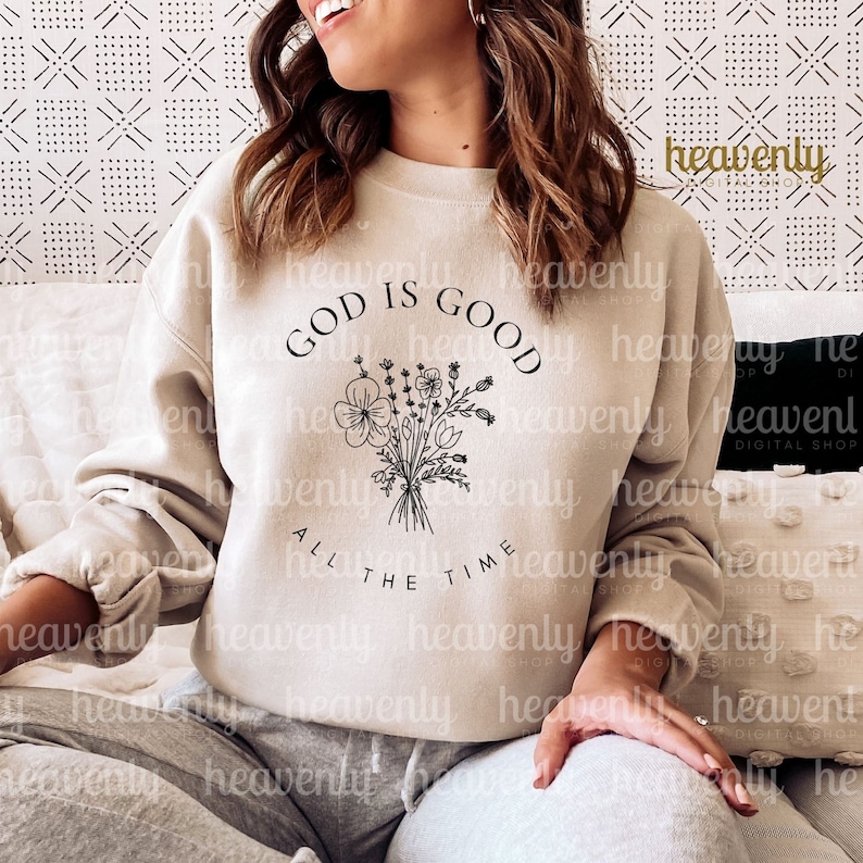 Peut inclure: Un sweat-shirt beige avec le texte "GOD IS GOOD ALL THE TIME" en lettres noires. Un dessin au trait noir d'un bouquet de fleurs est centr&eacute; au-dessus du texte.