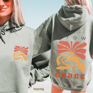 以下が含まれることがあります： 後ろに花柄と「Grow in Grace」の文字が入ったセージグリーンのパーカー。花はオレンジと赤です。