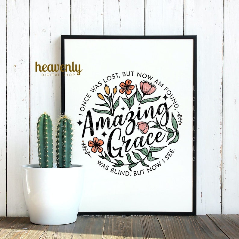 May include: A black framed print with a white background featuring a circle with the text "I once was lost, but now am found. Amazing Grace. Was blind, but now I see."  The text is surrounded by a wreath of green leaves and pink and orange flowers.