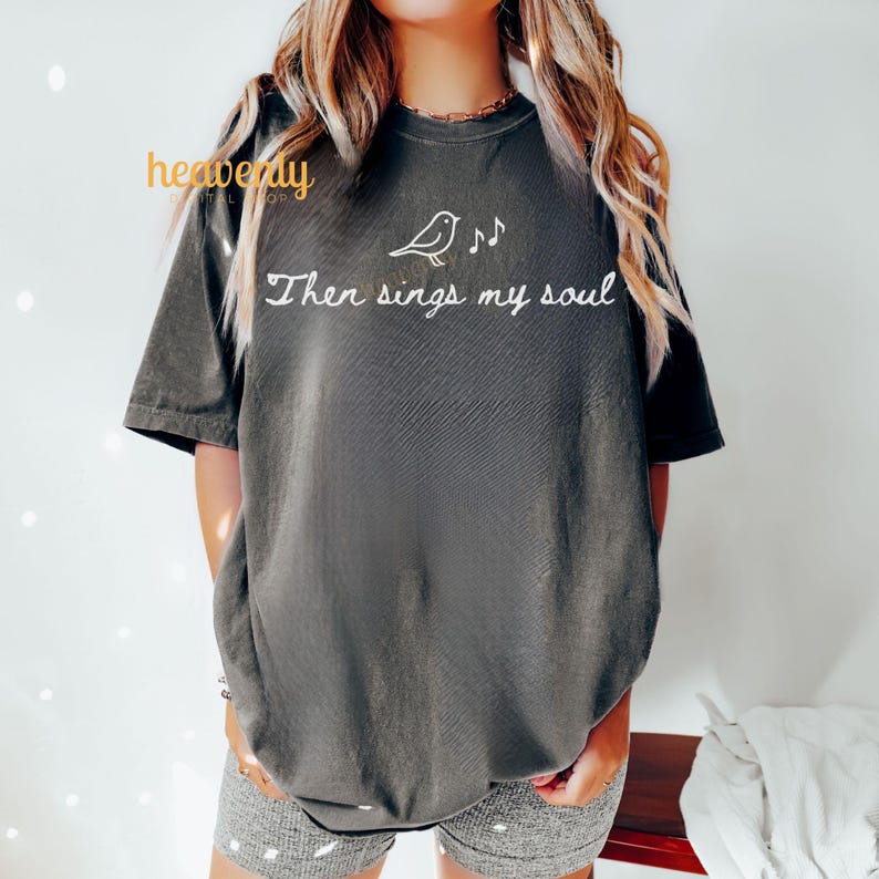 May include: Dark gray t-shirt with the text "Then sings my soul" and a bird with musical notes. The shirt has short sleeves and a relaxed fit. The shirt is made of a soft material.