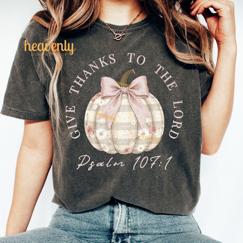 Puede incluir: Camiseta gris oscuro con un dise&ntilde;o de calabaza, lazo rosa y detalles florales. El texto dice "GIVE THANKS TO THE LORD" y "Psalm 107:1". La camiseta tiene un aspecto vintage y desgastado.