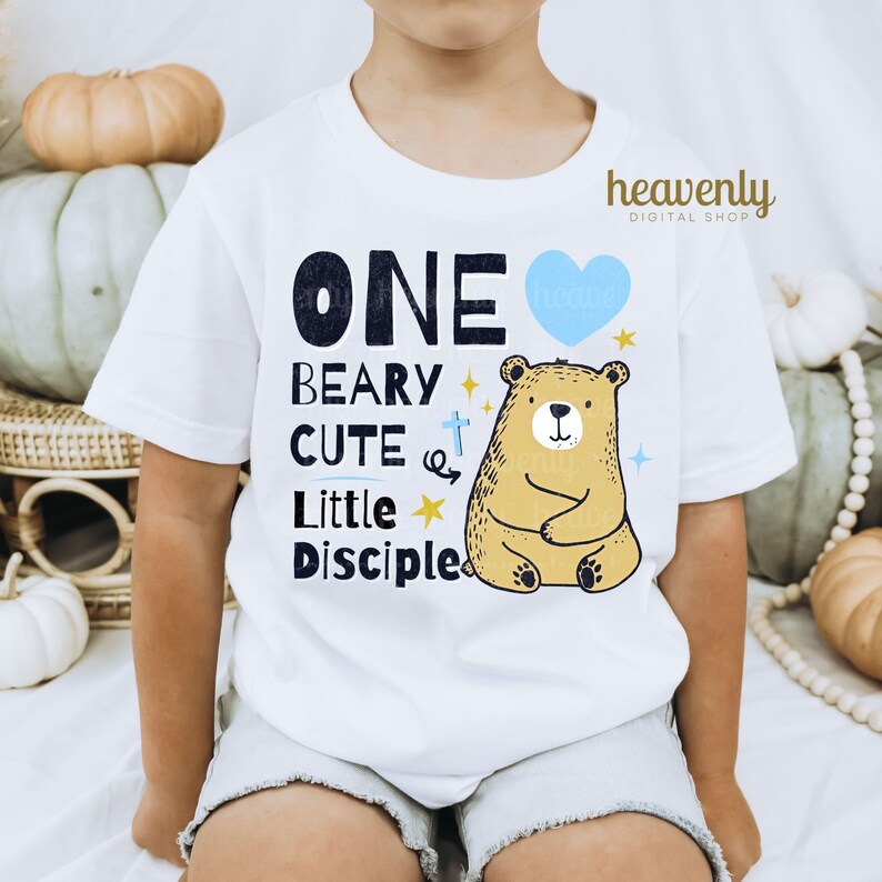 May include: White t-shirt with a blue heart, a brown bear, and the text "ONE BEARY CUTE LITTLE DISCIPLE".