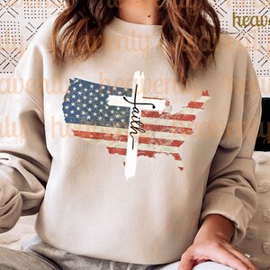 May include: A beige sweatshirt featuring a distressed American flag design and a white cross with the word "Faith" written on it.