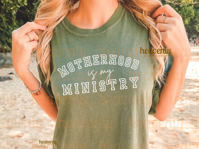 Pu&ograve; includere: Una donna indossa una maglietta verde con il testo "MOTHERHOOD is my MINISTRY" in bianco.