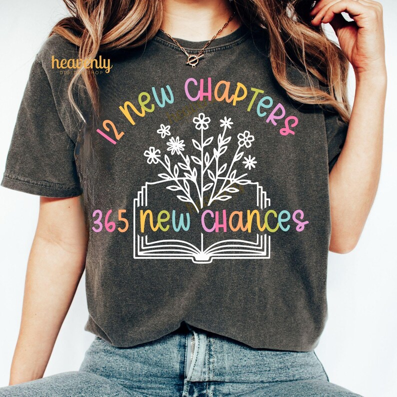 May include: A dark gray t-shirt with the text "12 new chapters 365 new chances" in colorful letters. The text is surrounded by a drawing of an open book with flowers growing out of it.