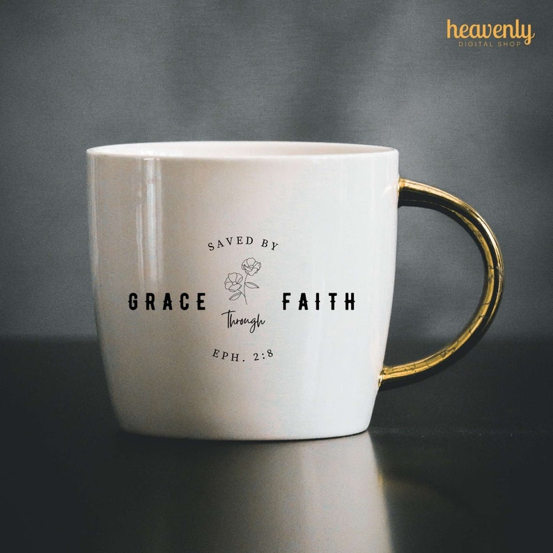 May include: White ceramic mug with a gold handle. The mug has a black graphic that says "Saved by Grace through Faith Eph. 2:8" with a small floral design.