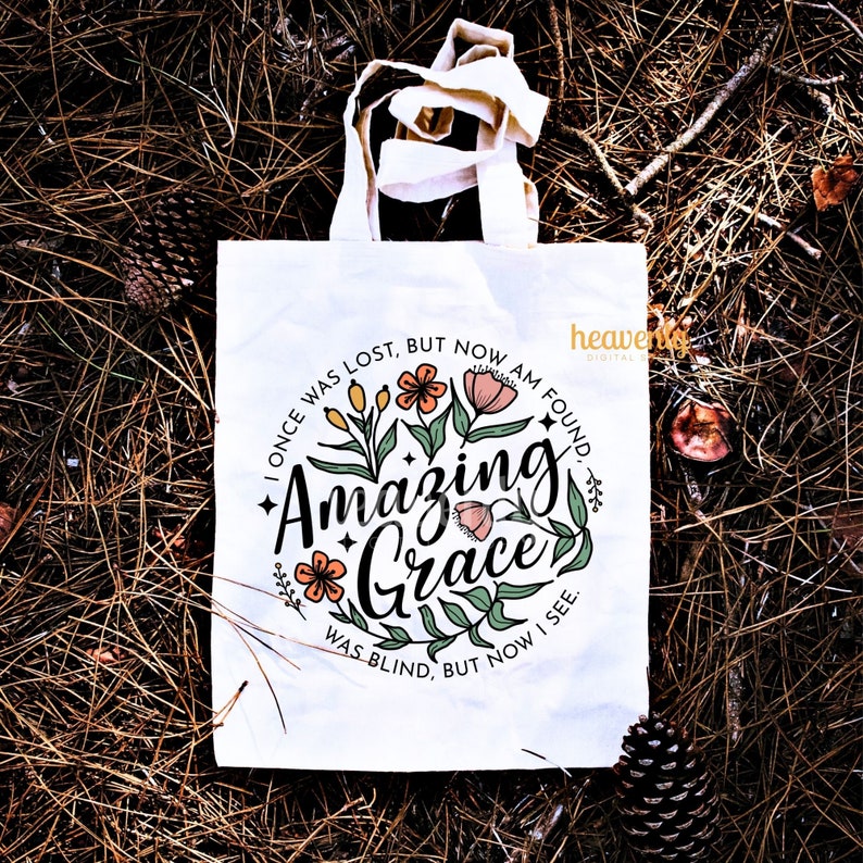 May include: White tote bag with a floral design and the text "I once was lost, but now am found. Amazing Grace. Was blind, but now I see."