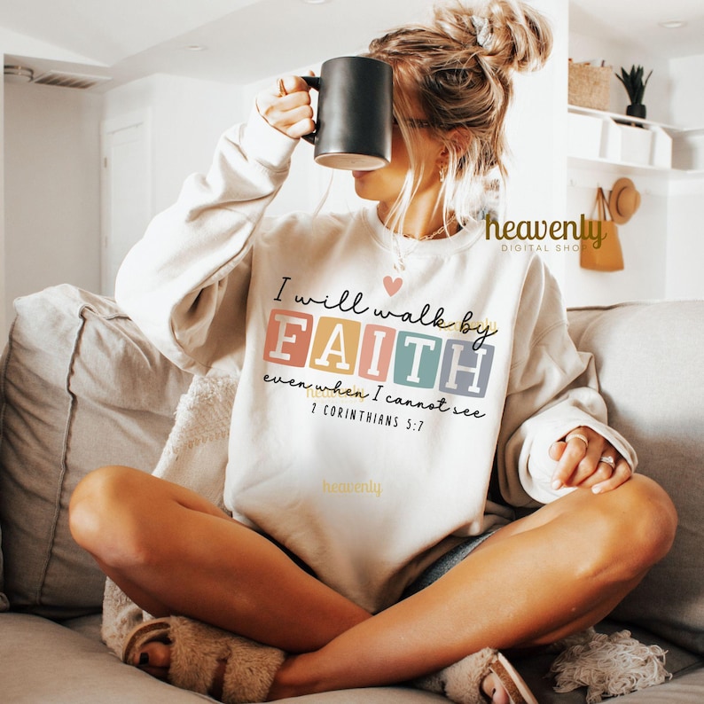 May include: A white sweatshirt with a colorful graphic that says "I will walk by FAITH even when I cannot see 2 Corinthians 5:7".
