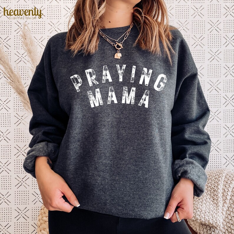 May include: A dark gray sweatshirt with the text "Praying Mama" in white distressed lettering.