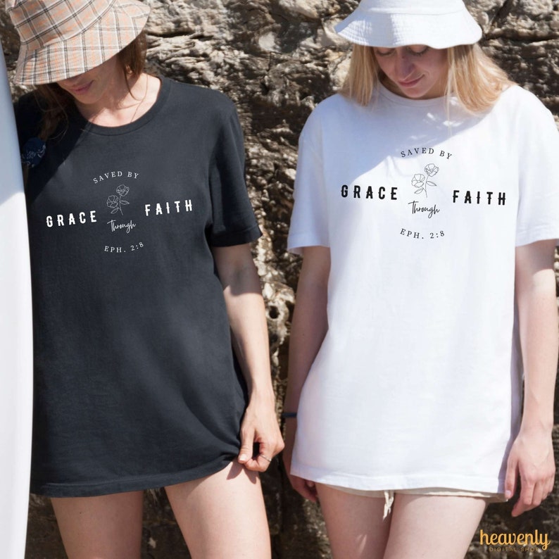 May include: Two people wearing black and white t-shirts with the text "SAVED BY GRACE Through FAITH EPH. 2:8" and a floral design.