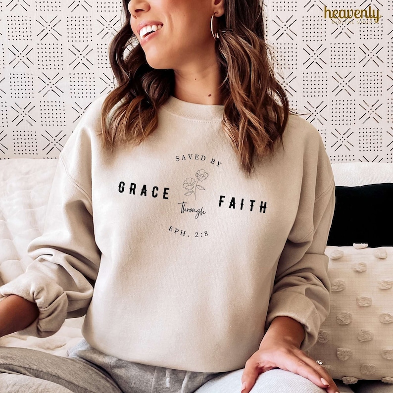 May include: A beige sweatshirt with the text "SAVED BY GRACE through FAITH" and the scripture reference "EPH. 2:8".