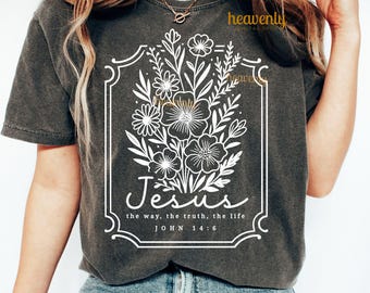 Peut inclure: T-shirt gris foncé avec un motif floral blanc dans un cadre rectangulaire. Le motif comprend le mot "Jésus" et le texte "le chemin, la vérité, la vie, Jean 14:6". Le t-shirt a des manches courtes et un col rond.
