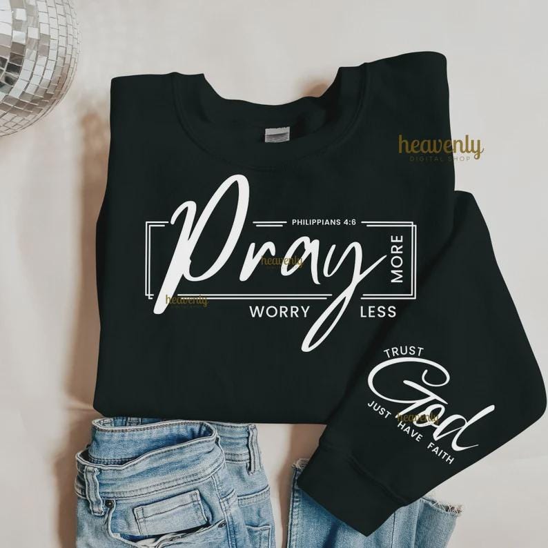 Pu&ograve; includere: Felpa nera con scritta bianca "Pray More, Worry Less" e "Trust God, Just Have Faith". La felpa &egrave; abbinata a jeans blu. Sono visibili anche le parole "heavenly digital shop".