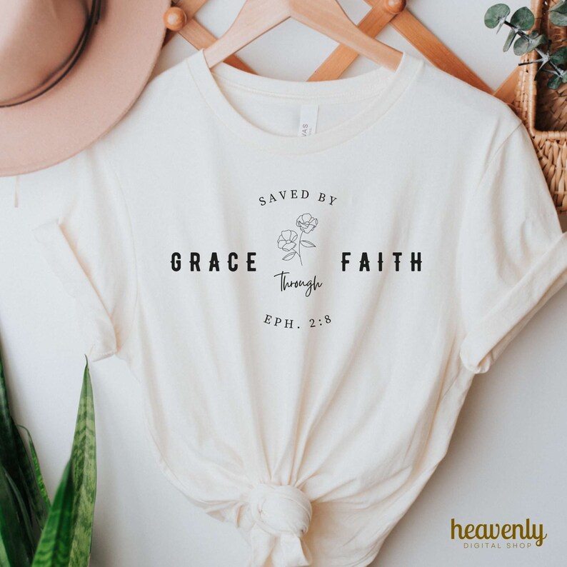 May include: A white t-shirt with the text "SAVED BY GRACE through FAITH EPH. 2:8" and a simple line drawing of two flowers.