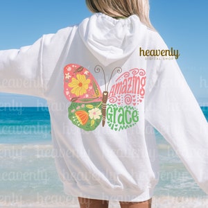 Puede incluir: Sudadera blanca con un gr&aacute;fico de mariposa rosa, verde y amarilla. La mariposa tiene las palabras "Amazing Grace" escritas en ella.
