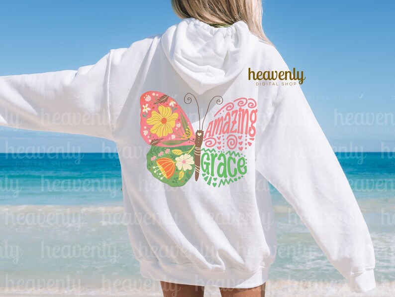 Puede incluir: Sudadera blanca con un gr&aacute;fico de mariposa rosa, verde y amarilla. La mariposa tiene las palabras "Amazing Grace" escritas en ella.