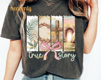 May include: A gray t-shirt with a watercolor design of a crown of thorns, a cross, a stone tomb, and a pink ribbon. The text "true story" is written below the design.