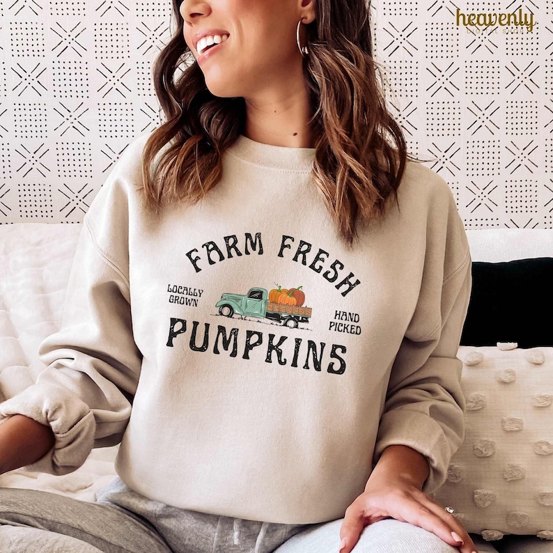 May include: Beige sweatshirt with a graphic that reads "Farm Fresh Pumpkins." The design features a teal truck carrying orange pumpkins, with text that says "Locally Grown" and "Hand Picked."