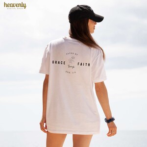 May include: White t-shirt with a black graphic that says "Saved by Grace through Faith Eph. 2:8".