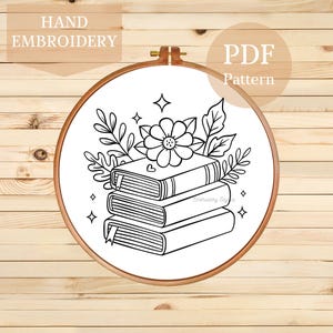 May include: An embroidery hoop featuring a black and white design of books, flowers, and leaves. The design includes the text "HAND EMBROIDERY" and "PDF Pattern". The hoop is set against a wooden background.